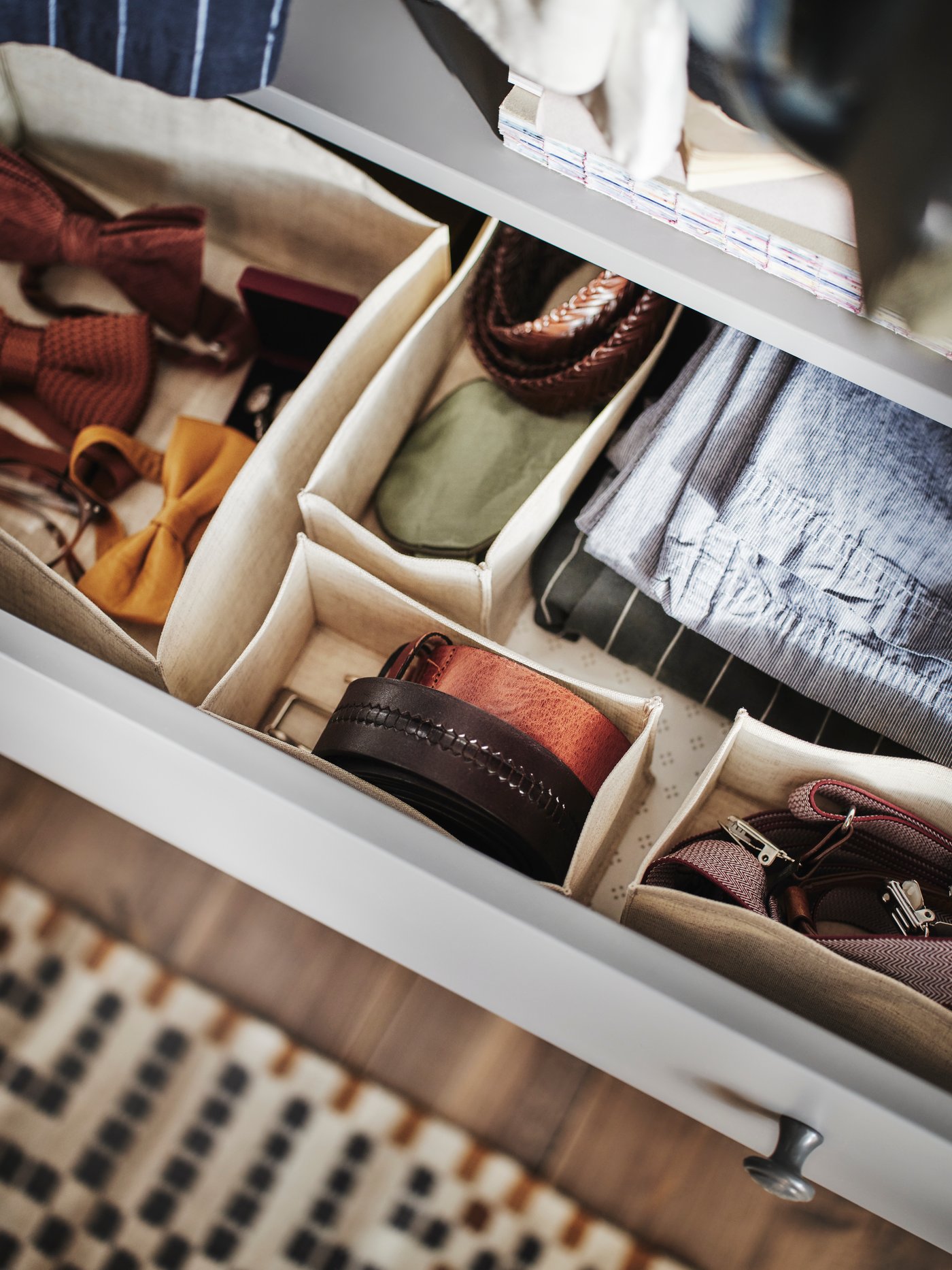 An open top drawer of a HAUGA chest with 3 drawers showing four BOLLÖSUND drawer organisers holding accessories inside.