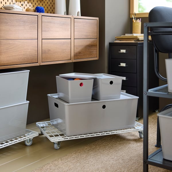 Close-up of light grey KUGGIS storage box under wall cabinets, storing office supplies.
