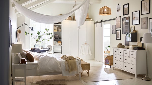 A white HEMNES bed covered in white DYTÅG bed linen and brown cushions with a DYTÅG curtain draped from the ceiling above it.