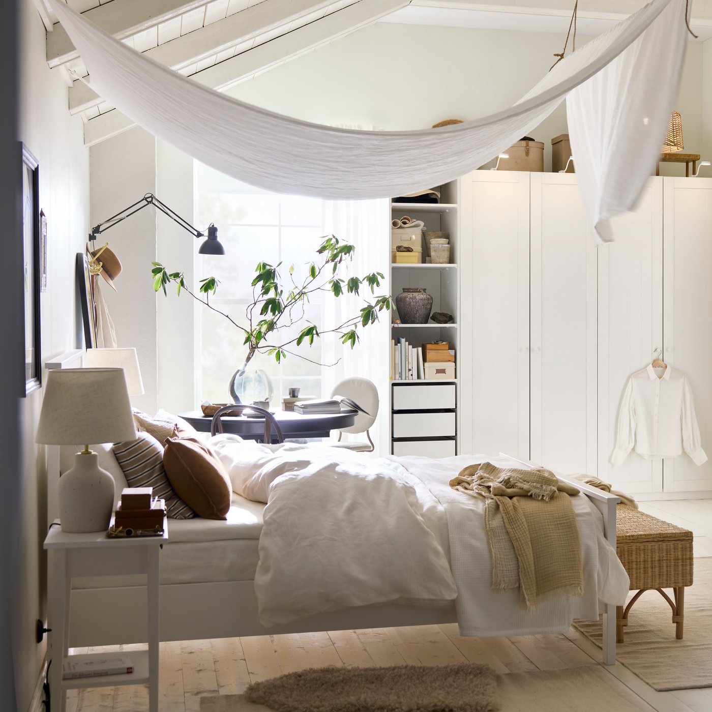 Un letto HEMNES bianco con biancheria da letto DYTÅG bianca, cuscini marroni e una tenda DYTÅG che scende dal soffitto formando dei drappeggi.