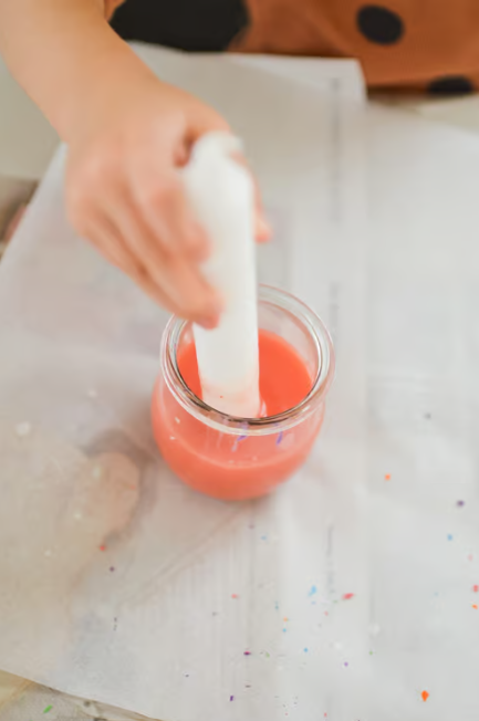 Eine Kerze wird in orangefarbene Wachsfarbe getaucht