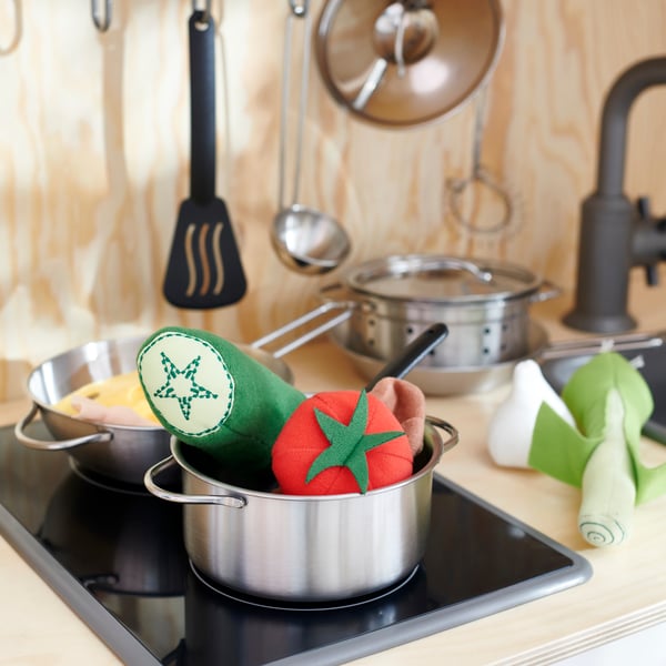 Close-up of DUKTIG play kitchen with two pots full of DUKTIG vegetables, utensils hanging in the back.