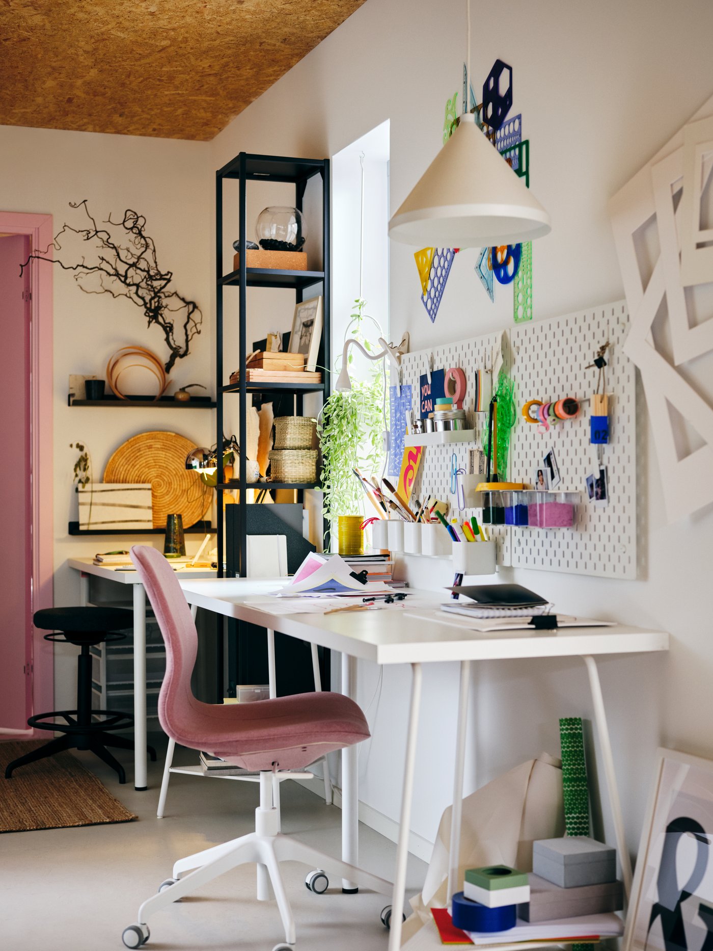 A room filled with IKEA products that focuses on the desk filled with stuff that also has a chair next to it.