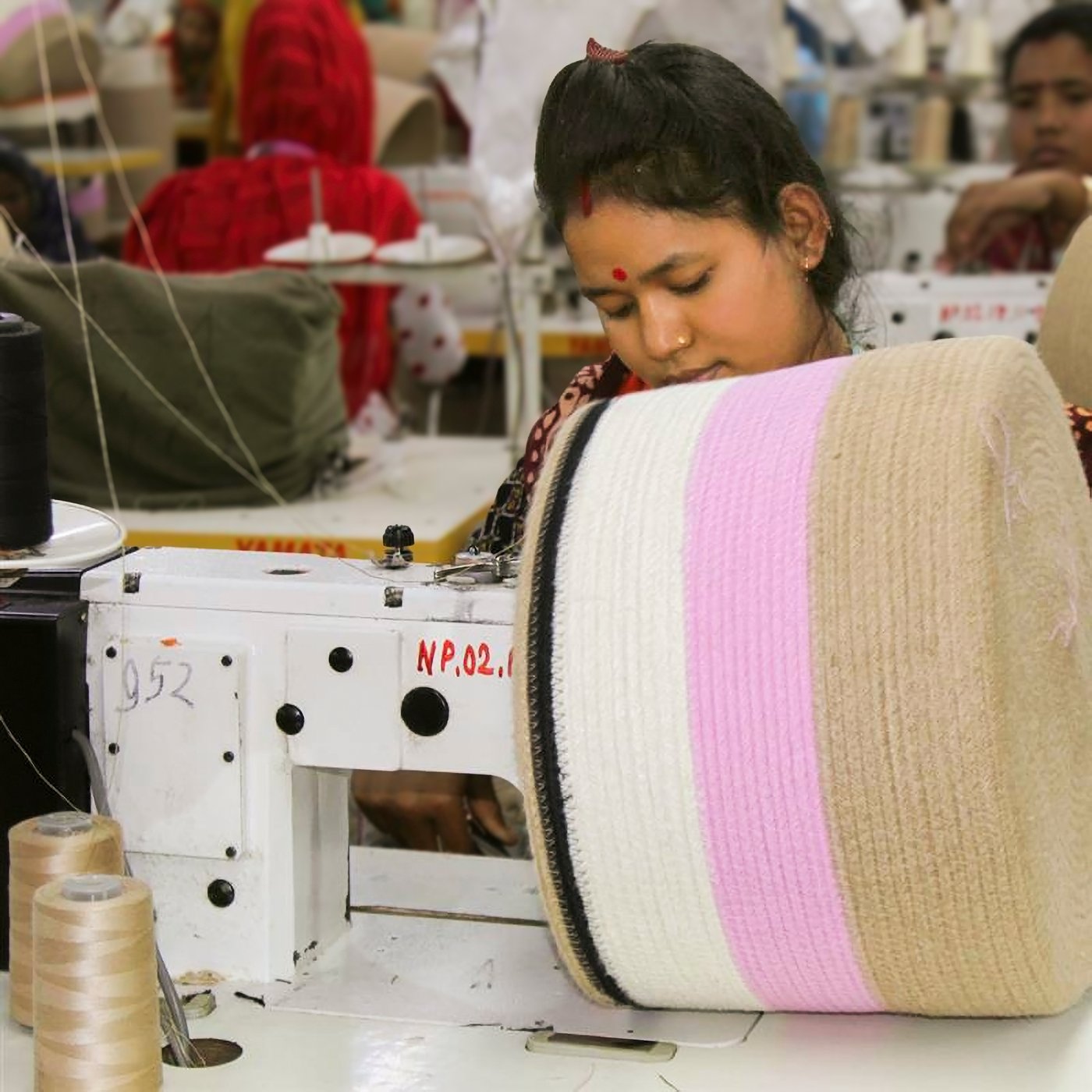 A worker operates a sewing machine, crafting a large spool of fabric with beige and pink stripes.