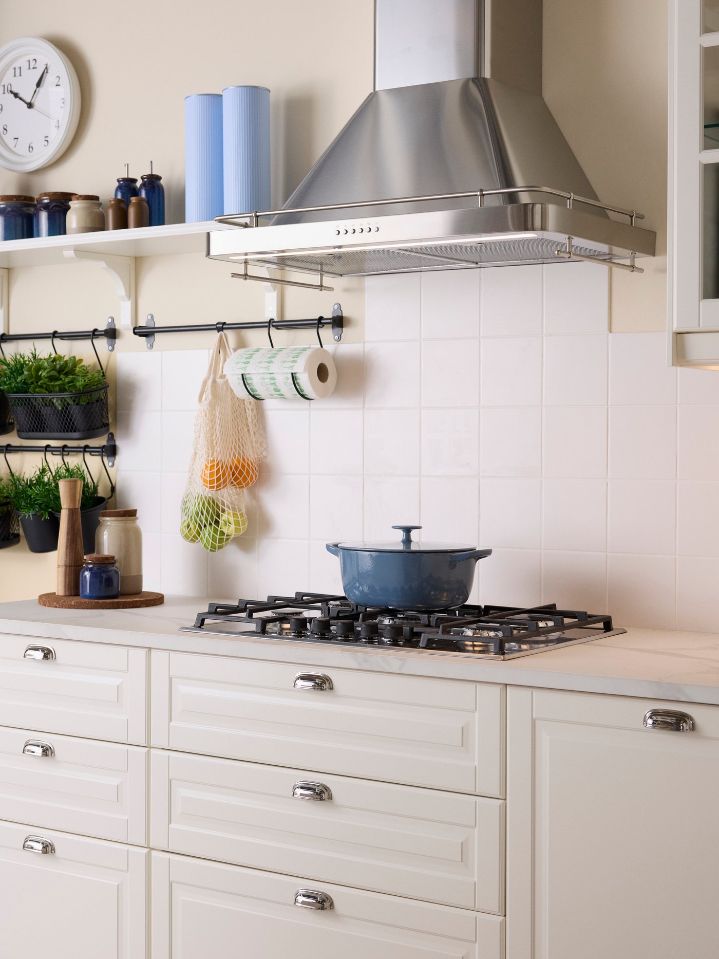 A white BODBYN kitchen close up with the gas hob and the traditional stainless steel extractor. There is a blue pot on the hob.