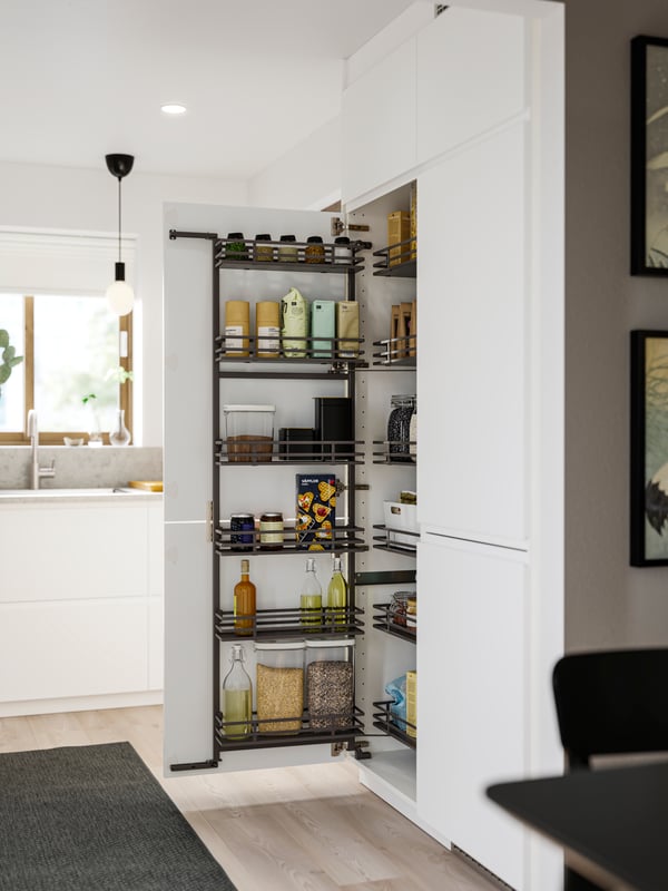 A kitchen with matte white VOXTORP fronts has an UTRUSTA pull-out larder with food packages and containers stored inside.