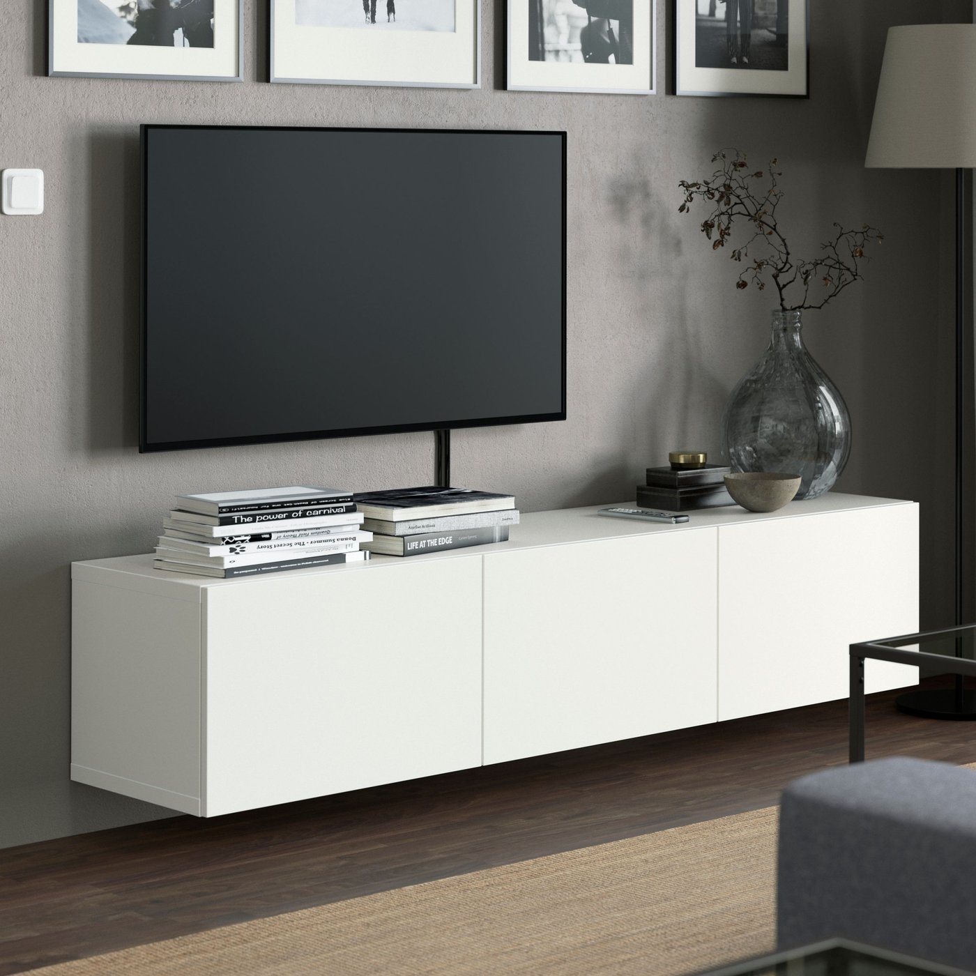 En låg, lång, vit tv-bänk som hänger på en grå vägg med en vägghängd tv. 