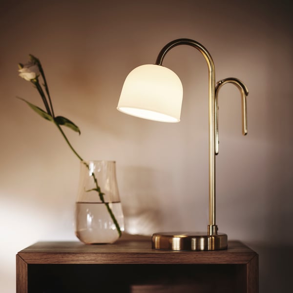 Close-up of TVÅMASTAD LED portable lamp in front of glass vase with a flower. Soft light all around.