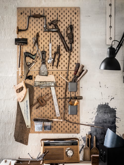 Traditional workspace close-up of a beige pegboard made out of fibreboard with multiple hooks and containers with lid.