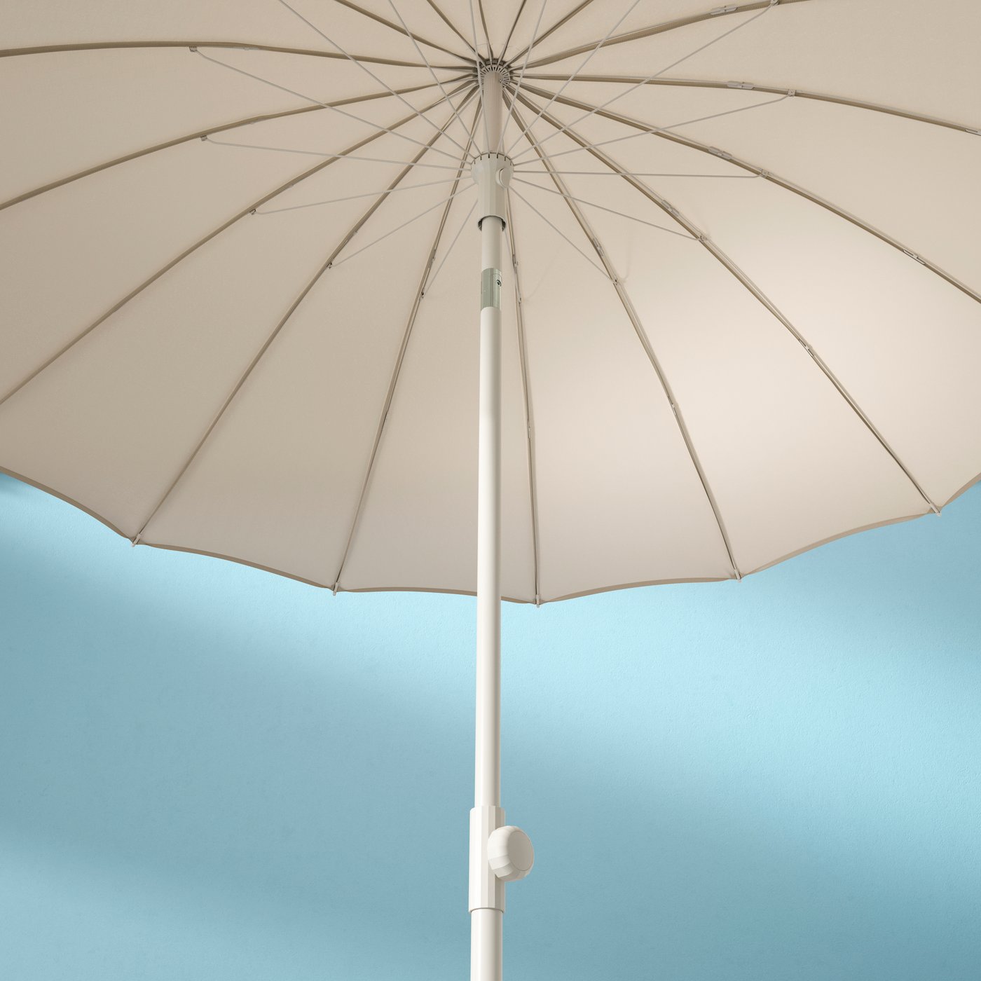 Un grand parasol IKEA beige, doté d’un fin mât blanc, se déploie sur un fond turquoise.