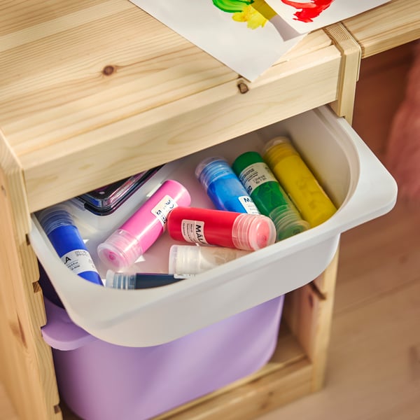 A TROFAST desk in pine with an open drawer showing a storage tray filled with colourful paint tubes and a purple storage box.