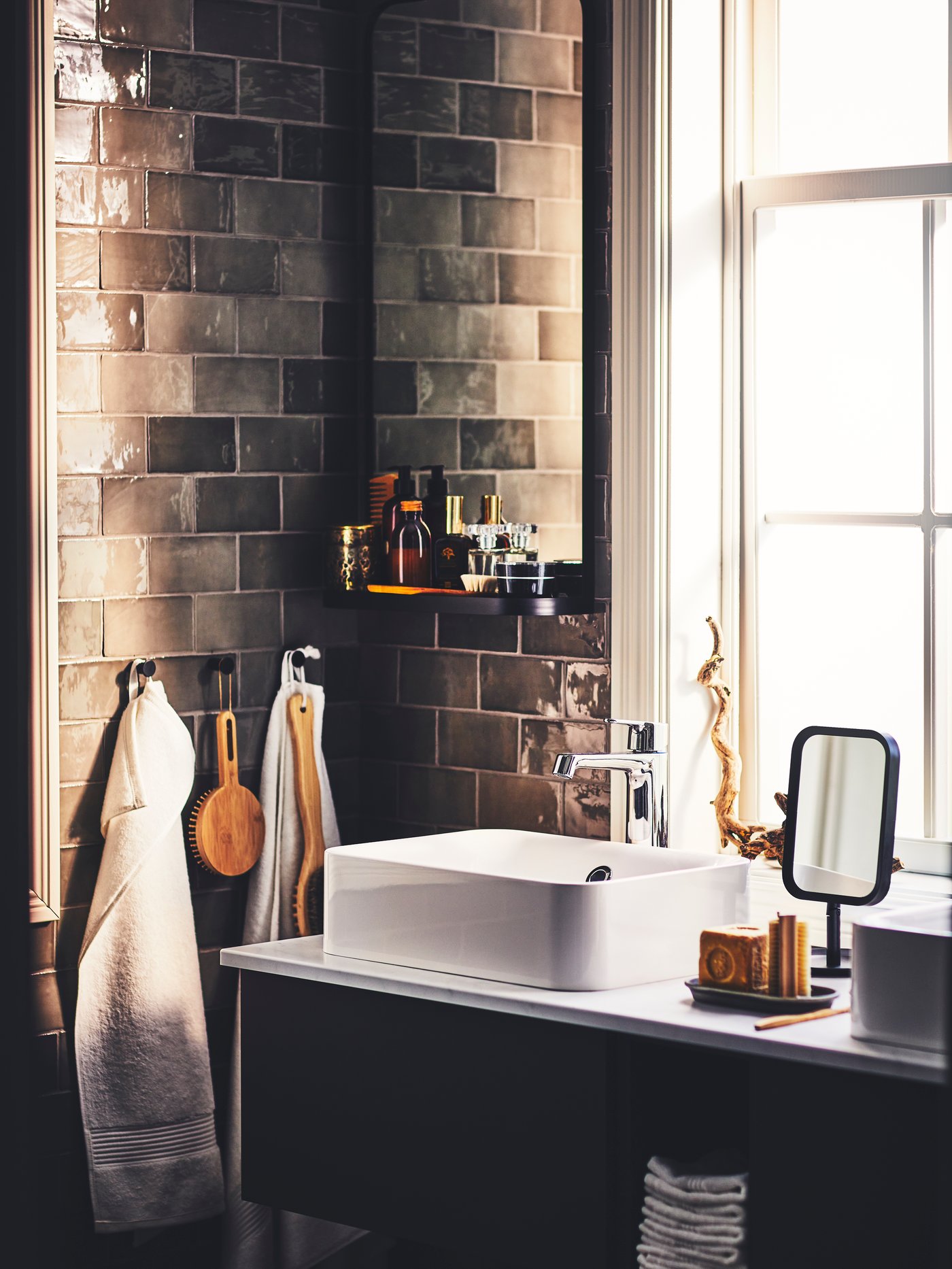 A bathroom with a dark grey GODMORGON wash-stand, a black LINDBYN table mirror and items hung from SKOGSVIKEN hooks.