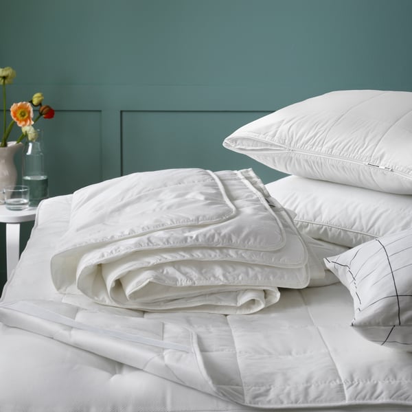 EIn Bett auf dem ein Matratzenschutz und verschiedene Duvets und Kissen liegen