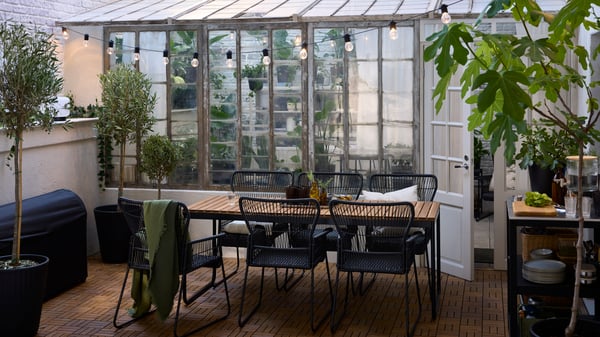 A VÄSMAN extendable table and six TALLSKÄR chairs with armrests on RUNNEN acacia outdoor floor decking in an outdoor setting.