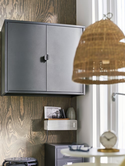 A cabinet with two doors is mounted on a wall, with a WiFi speaker mounted below, and a pendant lamp shade hanging in front.