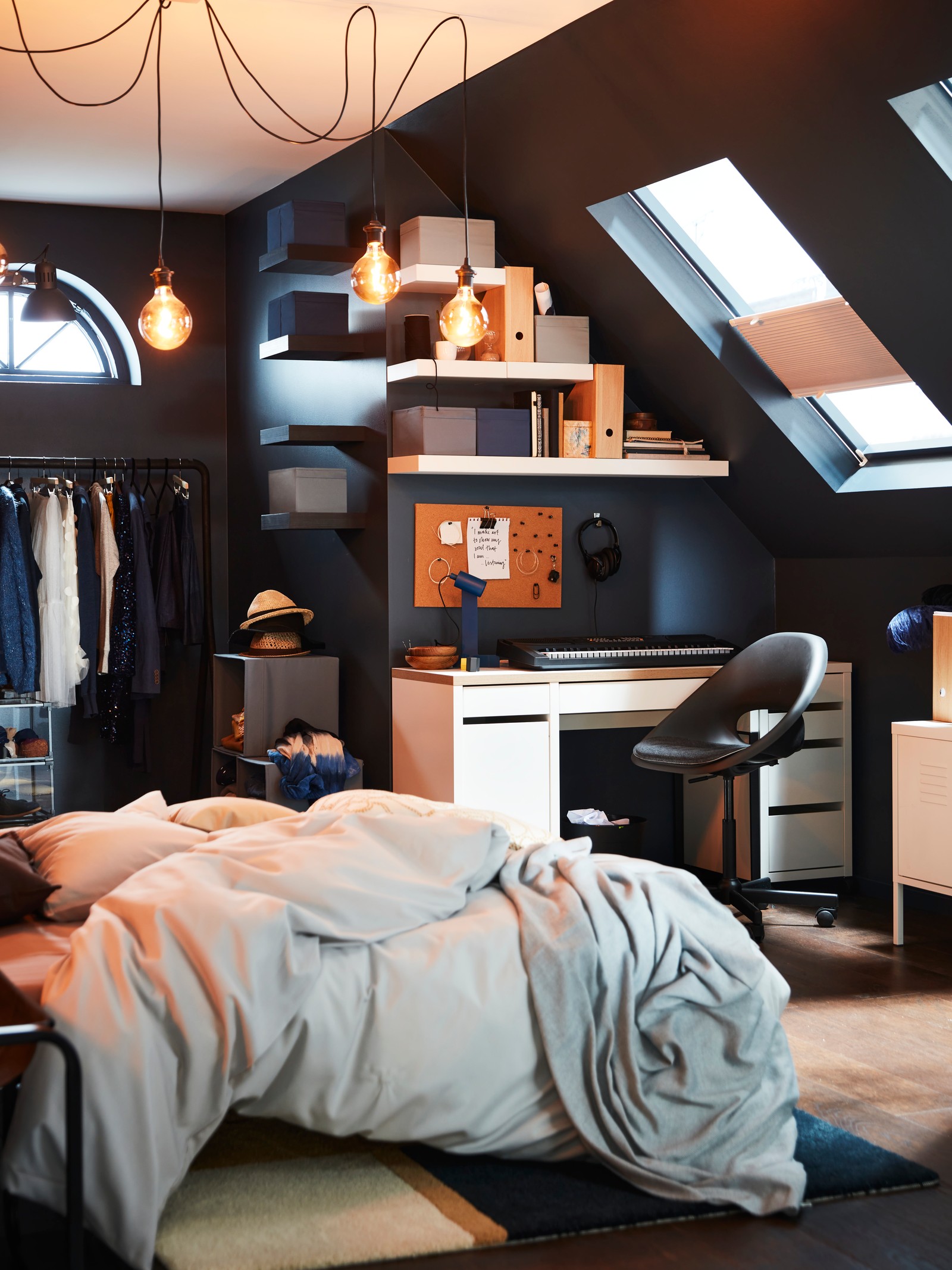 Podkrovní místnost s psacím stolem MICKE v rohu a postelí s povlečením PILTANDVINGE, nad kterou visí žárovky MOLNART.