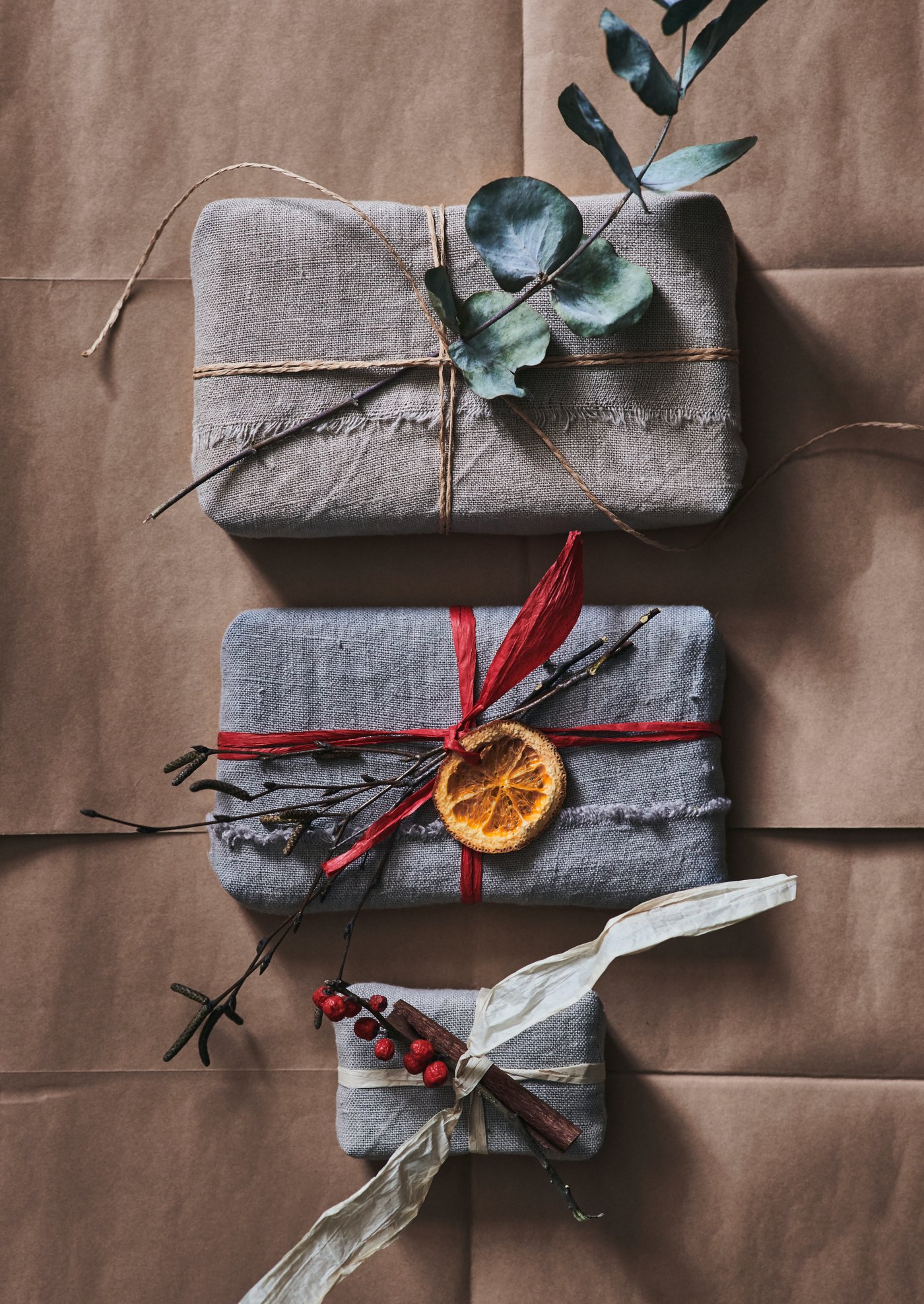 Enkelt inslagna paket på rad med små dekorationer som en eukalyptusgren och en torkad apelsinskiva.