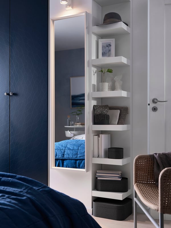 An einer Wand steht ein Regal mit Regalen daneben. Vor dem Kasten steht ein Bett mit blauer Bettwäsche.