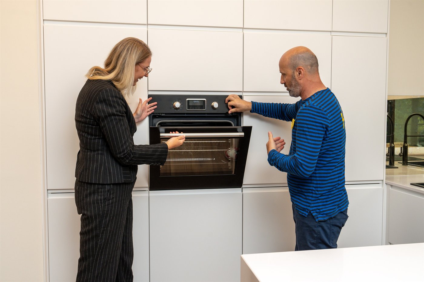 Man sieht eine Frau und einen IKEA Mitarbeiter wie sie den Backofen in einer weißen IKEA Küche öffnen und miteinander sprechen.