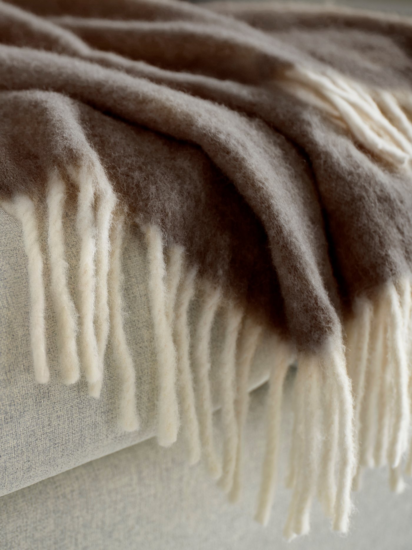En mjuk filt i beige och bruna nyanser ligger vikt med fransar synliga.