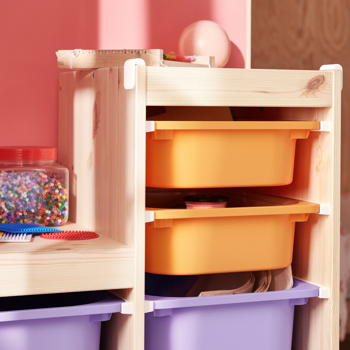 A light white stained pine TROFAST frame holds light orange and lilac boxes filled with art materials and toys.