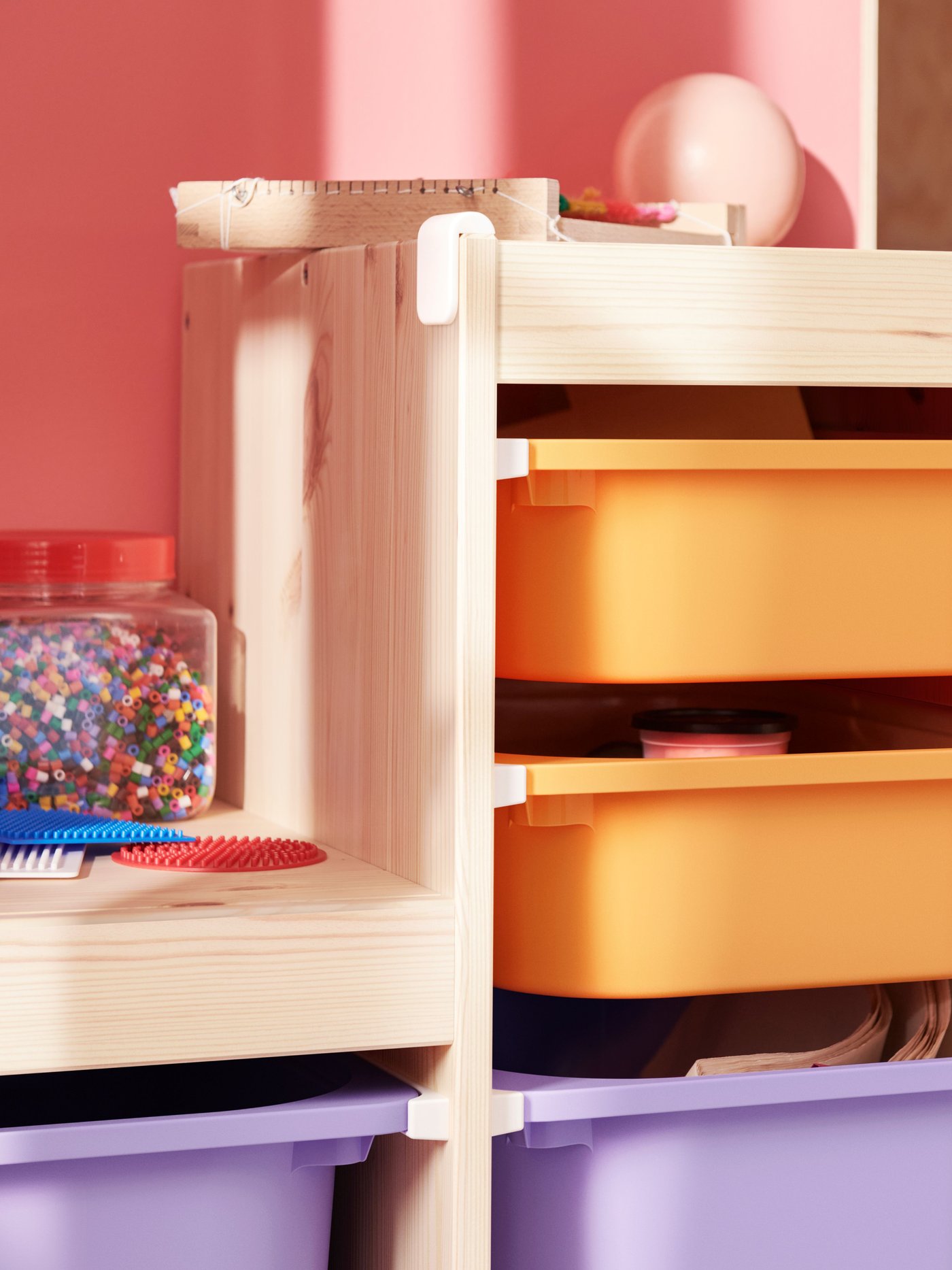 A light white stained pine TROFAST frame holds light orange and lilac boxes filled with art materials and toys.