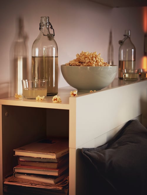 Fotografie cu o tăblie cu un compartiment de depozitare, care conține cărți și o sticlă cu dop și un bol cu popcorn deasupra.