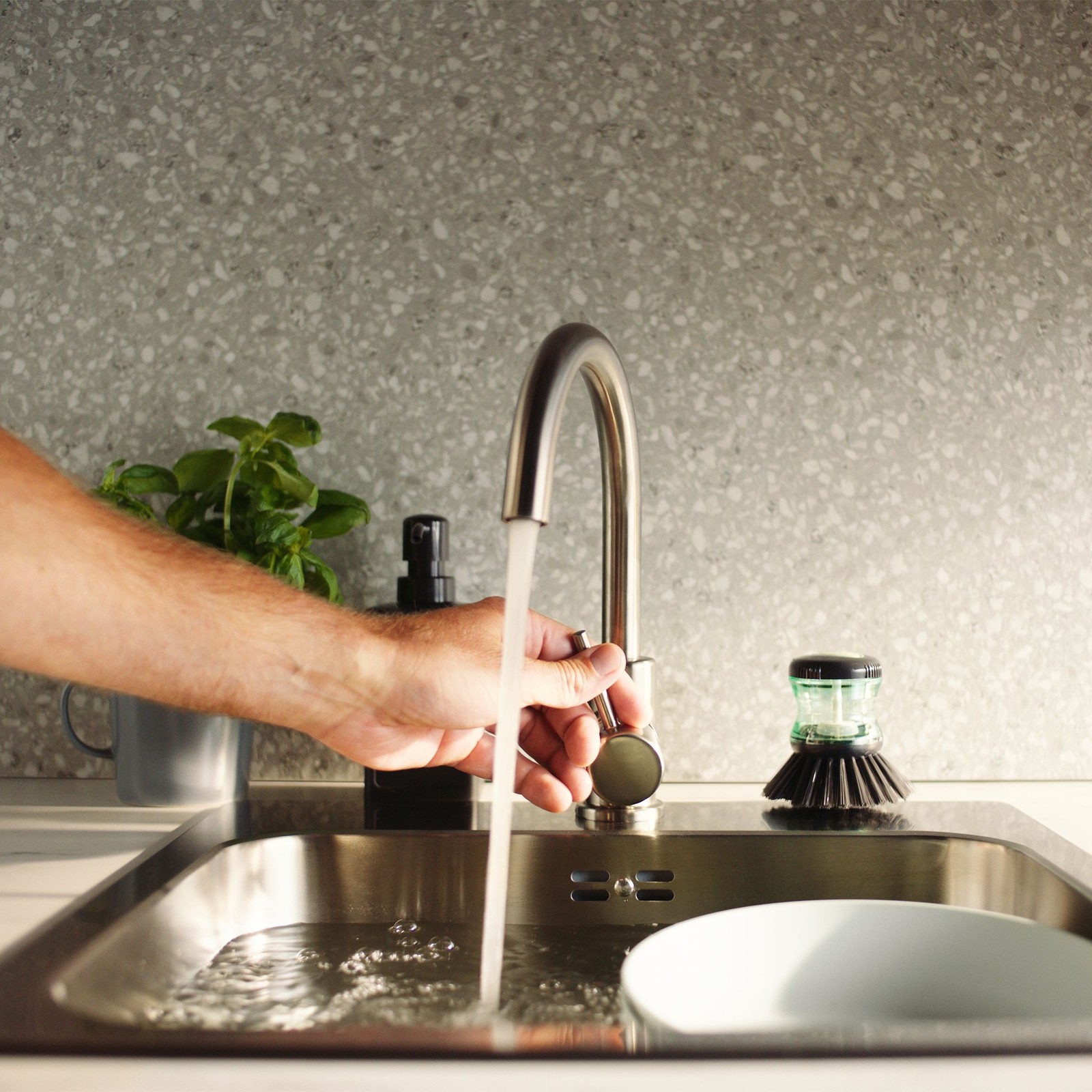 O persoană a dat drumul la apă, care curge din robinet în chiuvetă, într-o bucătărie.