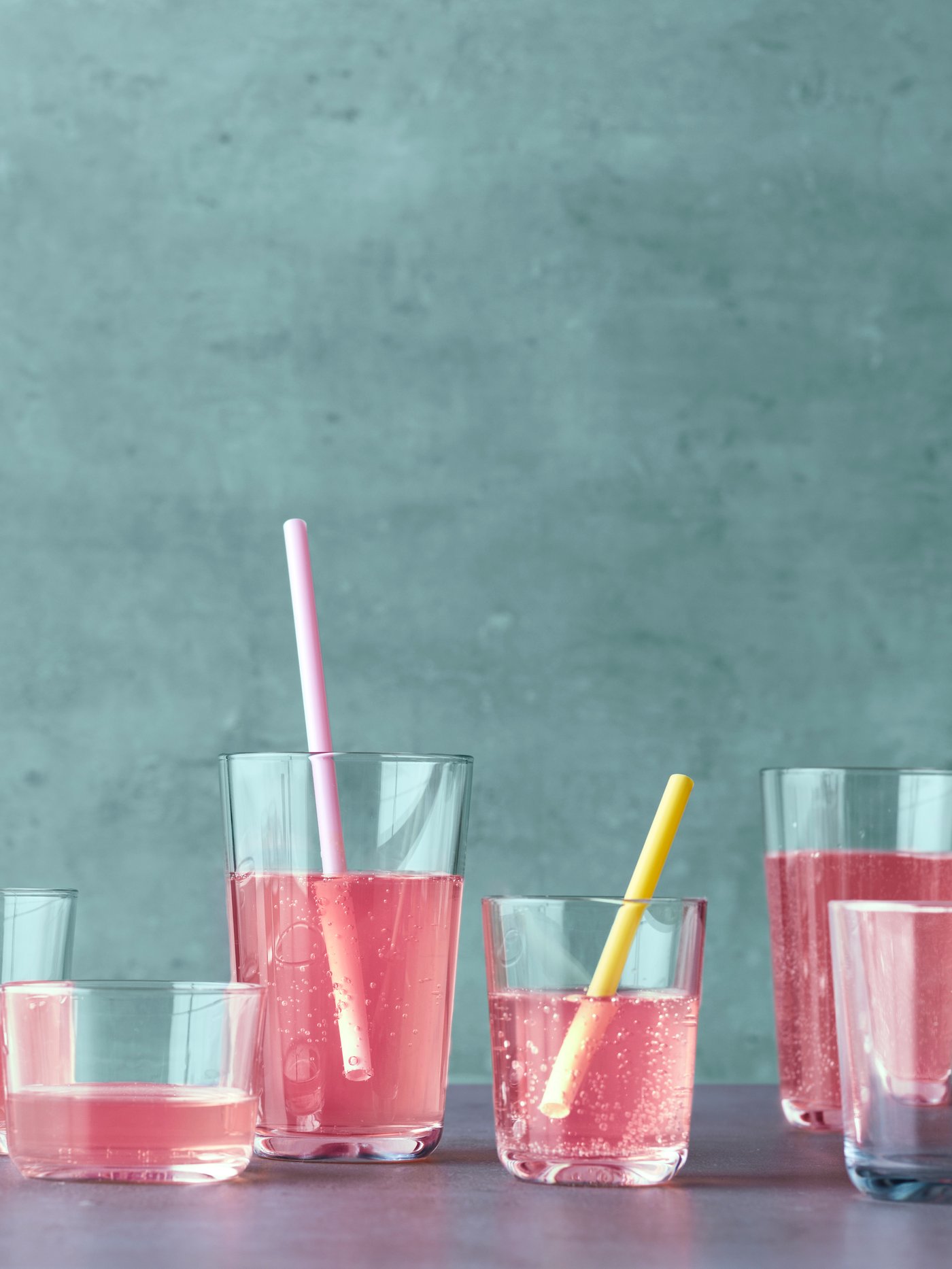 Fotografía de varios vasos de diferentes formas y tamaños que contienen un líquido rosa, dos de ellos con pajitas.