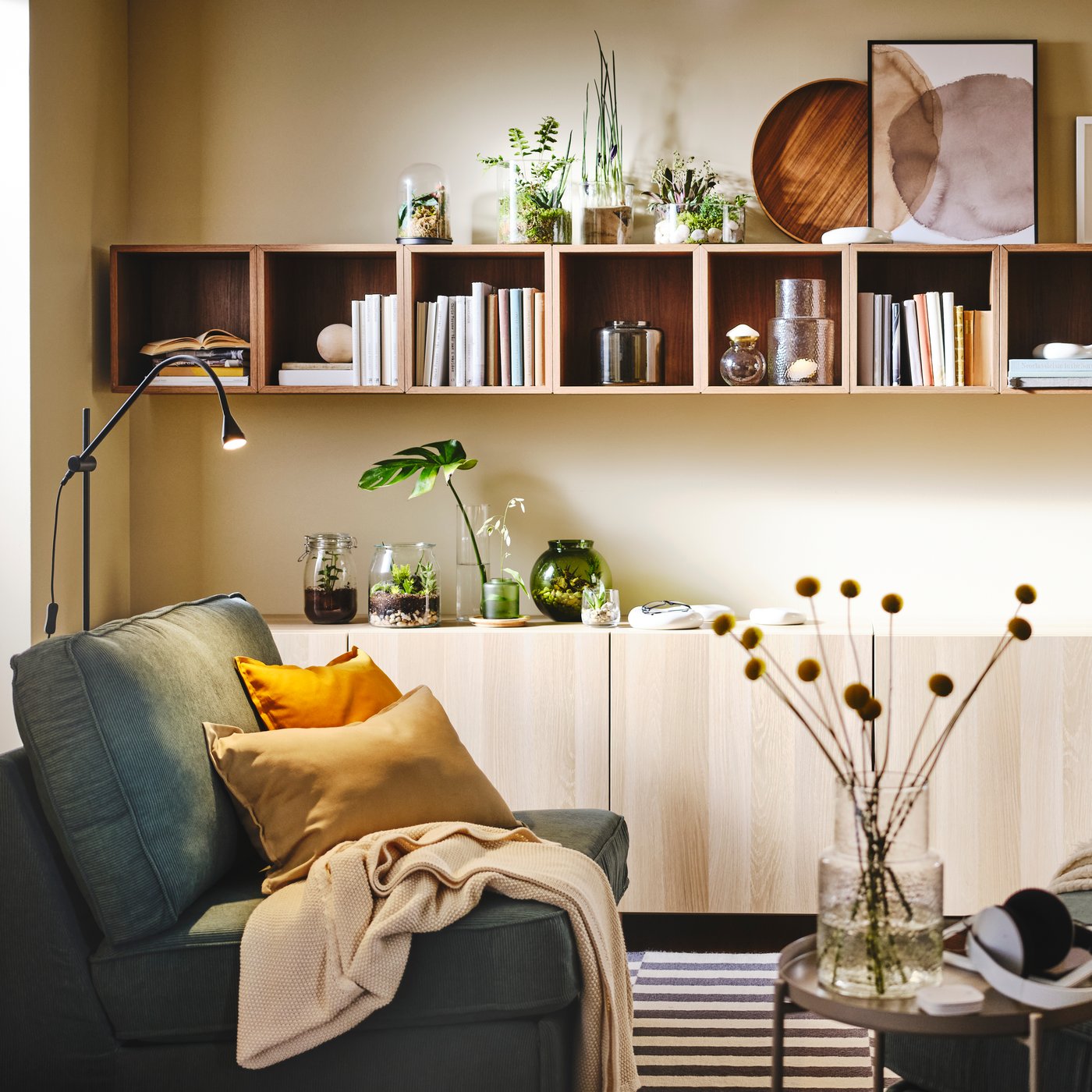 A bright living room with sofa modules round a coffee table, and a long row of books-and-deco-filled EKET cabinets on a wall.