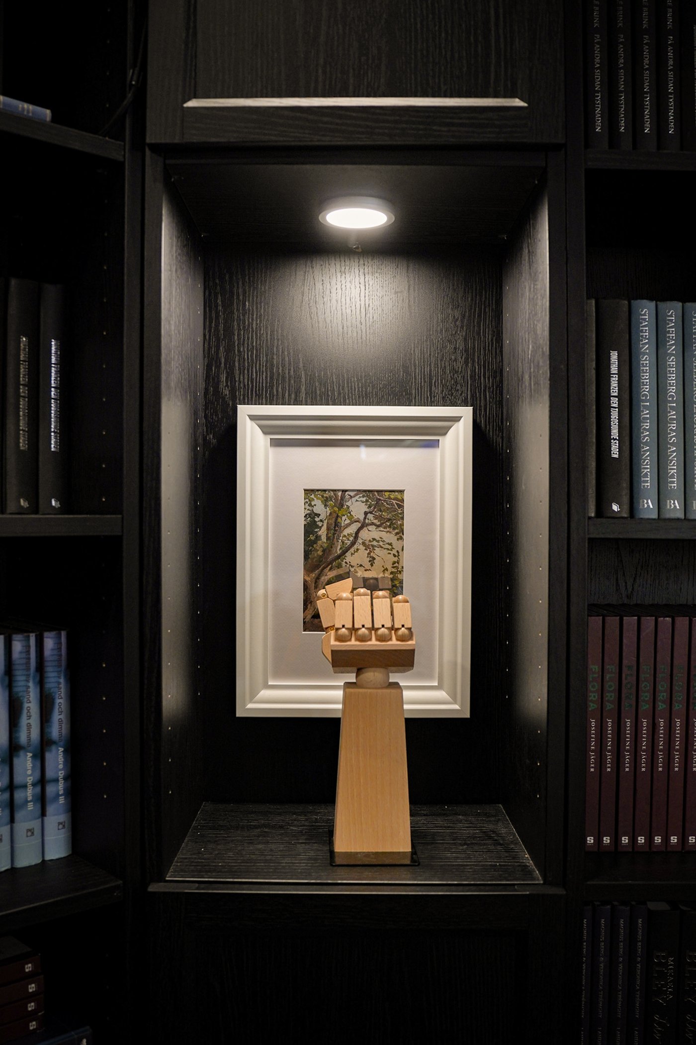 Curious Library room setting at IKEA Tampines, featuring a wooden decorative hand in front of a white VASTENHED frame, in the shelf of a black oak effect BILLY bookcase.