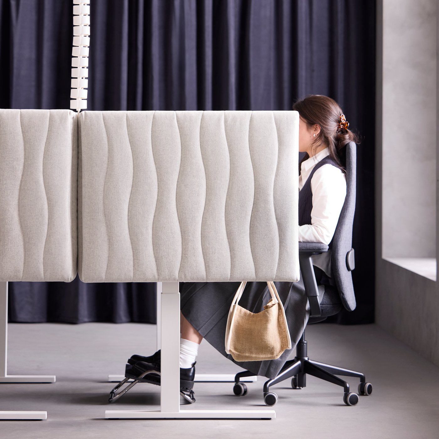 Office scene with a person sitting at a workspace separated by a beige MITTZON acoustic screen in Gunnared beige.