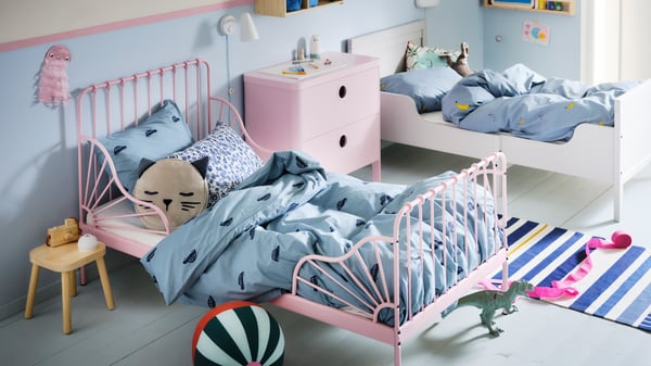 Een kinderkamer met een lichtroze MINNEN meegroeibed en een wit bed met blauw VÄNKRETS en BARNDRÖM beddengoed.