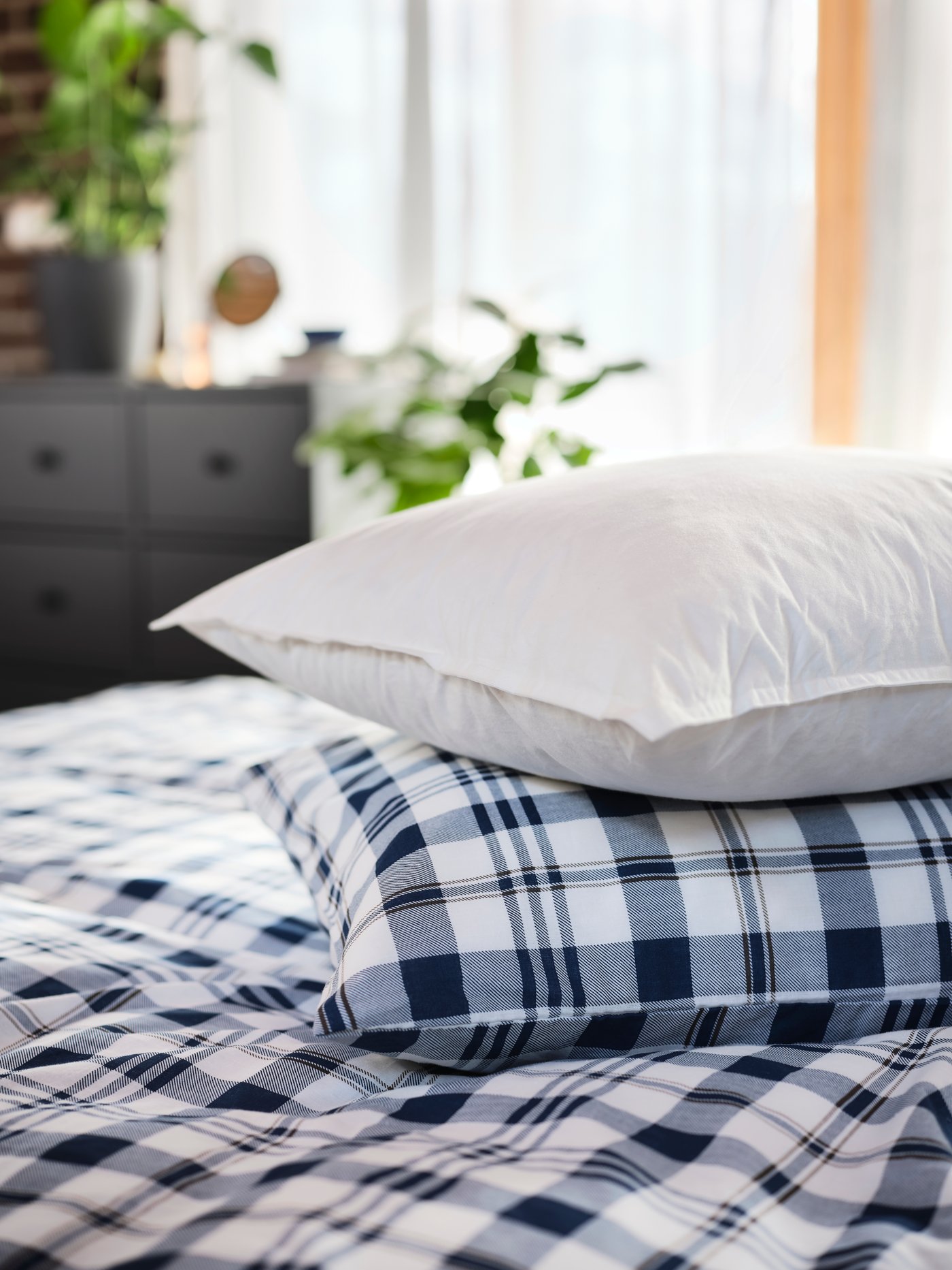 A high, white LUNDTRAV pillow without pillowcase on top of a pillow with a pillowcase and quilt cover with white-blue checks.