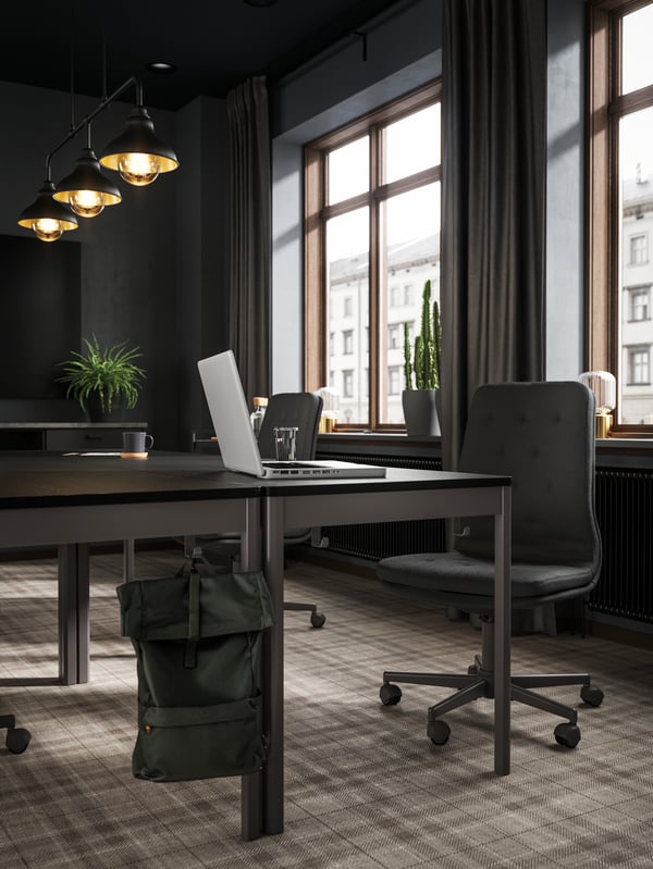 IDÅSEN black /dark grey tables and MULLFJÄLLET chair, an olive-green backpack in the front and windows in the background.