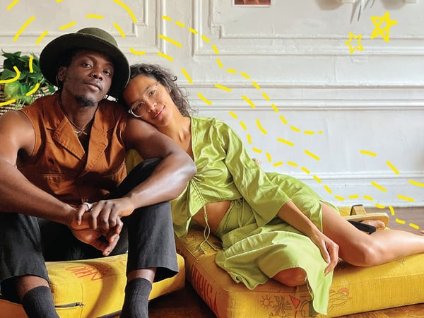 A man and a woman sitting on yellow cushions on the living room floor.