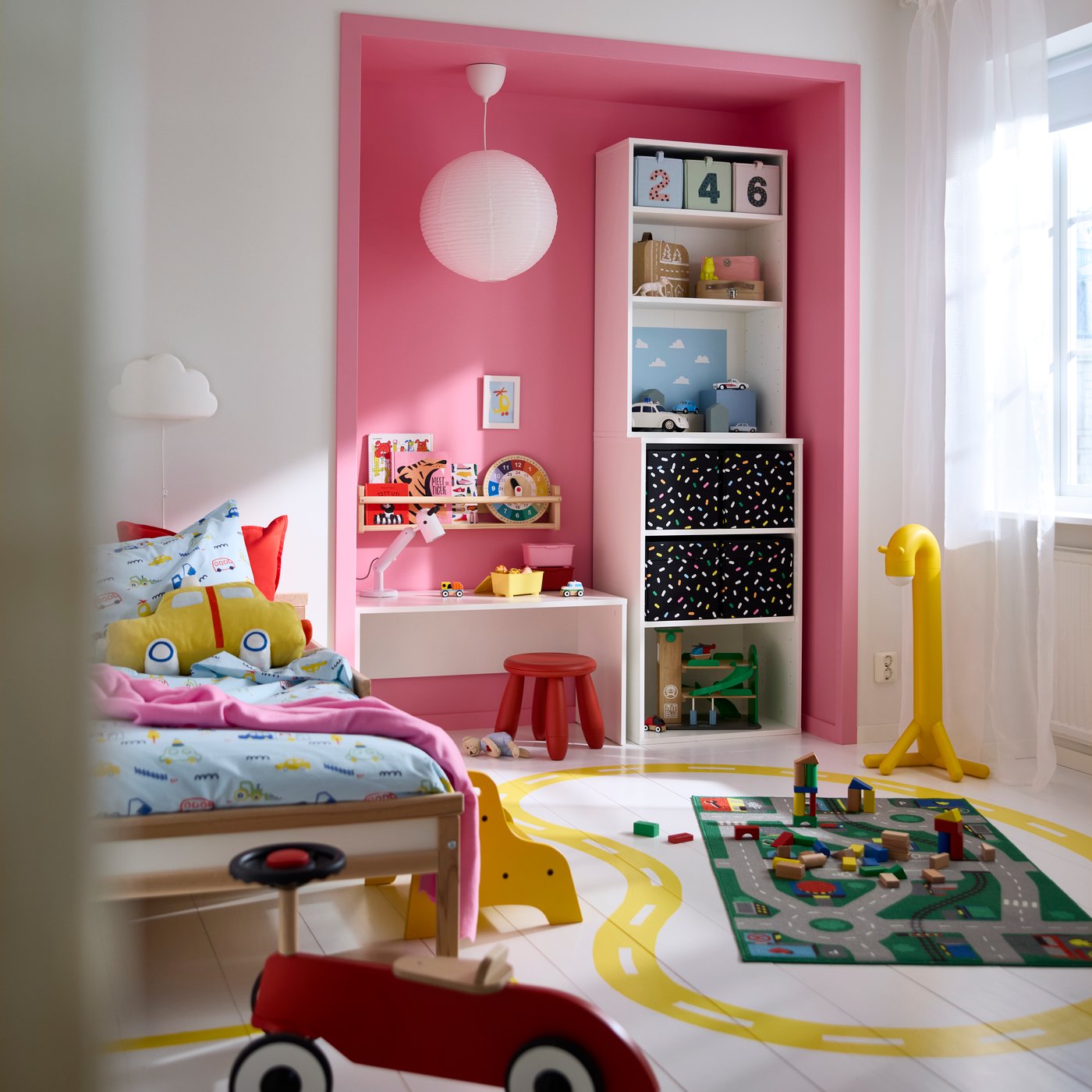A colourful playroom featuring a LASTARE wardrobe combination with boxes and toys on the shelves, beside a bed and play area.
