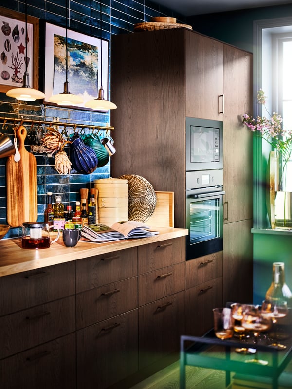 A SINARP kitchen with a blue-green tiled wall, with pendant lamps above a worktop with kitchen accessories.