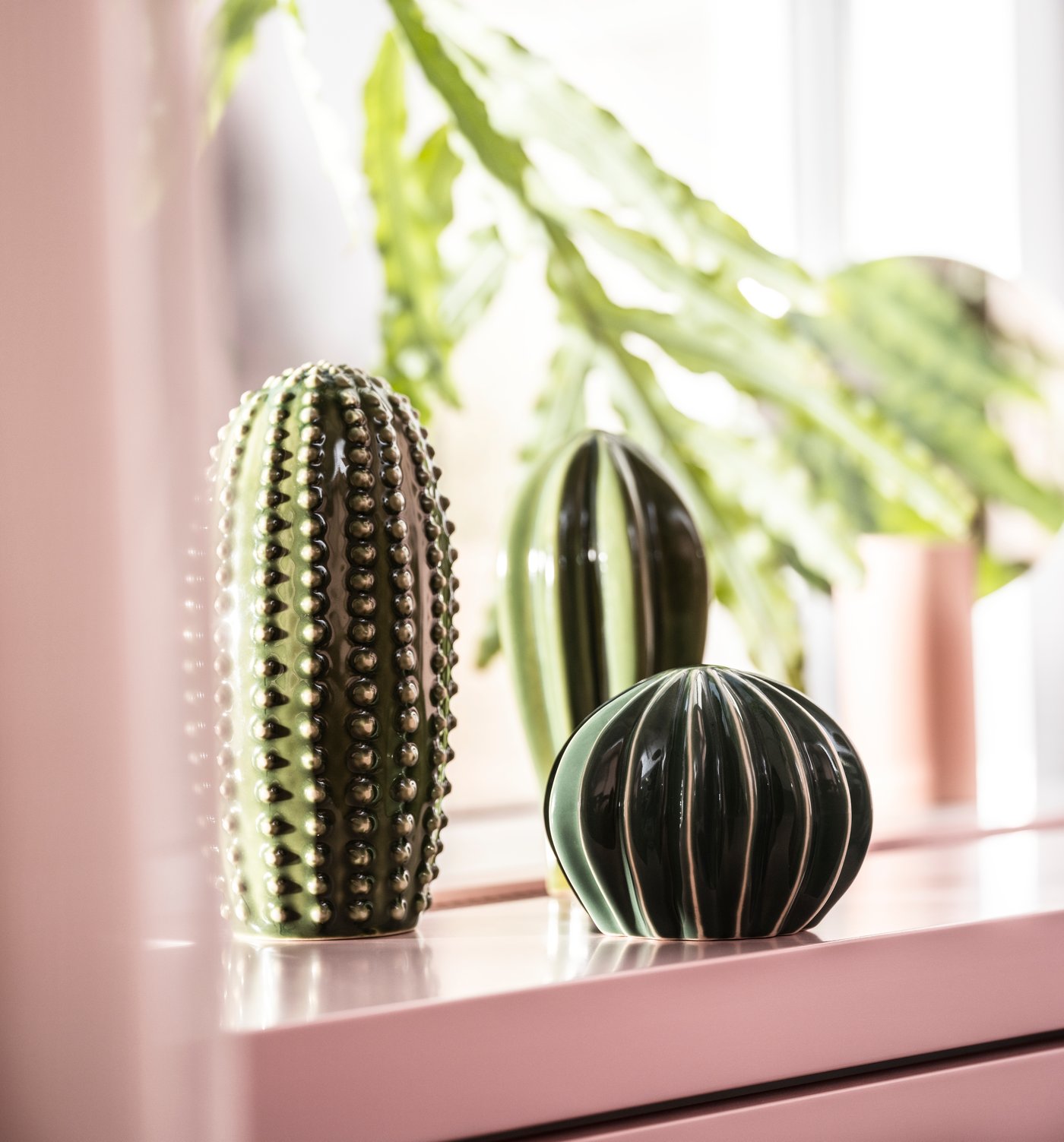 Un set di tre decorazioni verdi SJÄLSLIGT su un davanzale rosa.