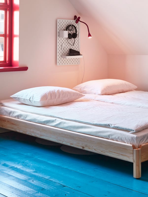 A bedroom with sloped ceiling and a small window showing two UTÅKER beds next to each other with white bedlinen on top.