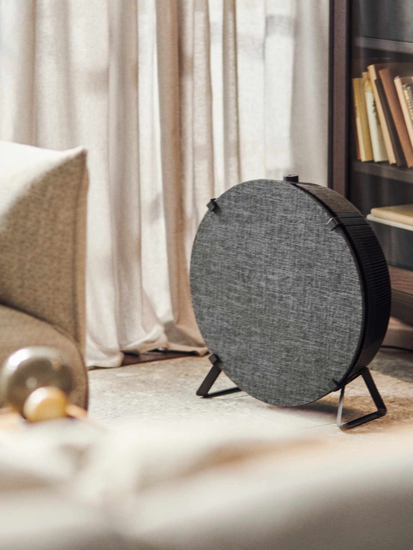 Chytrá čistička vzduchu STARKVIND v černé barvě stojí na podlaze před knihovnou.