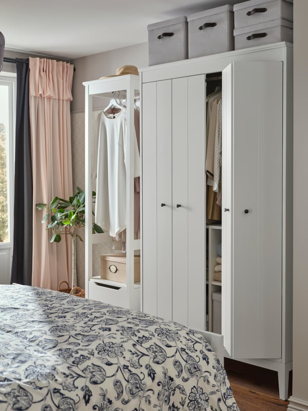 A tall IDANÄS wardrobe with boxes on top in a traditional, bright bedroom.