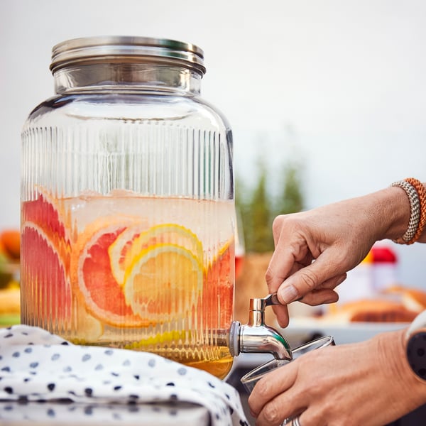 Woman's hand holding a glass from VARDAGEN jar with tap