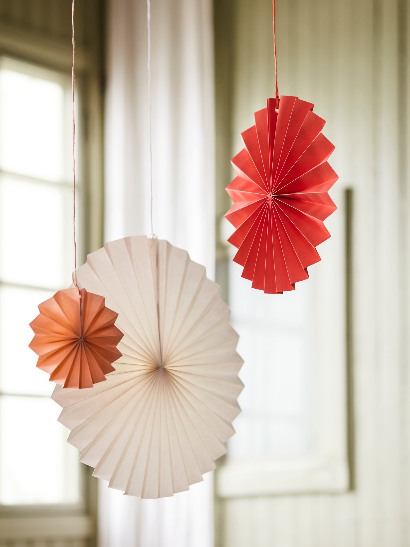 ANLEDNING hanging decorations in round paper fans made in white, apricot and red hanging by some string in a spacious room.