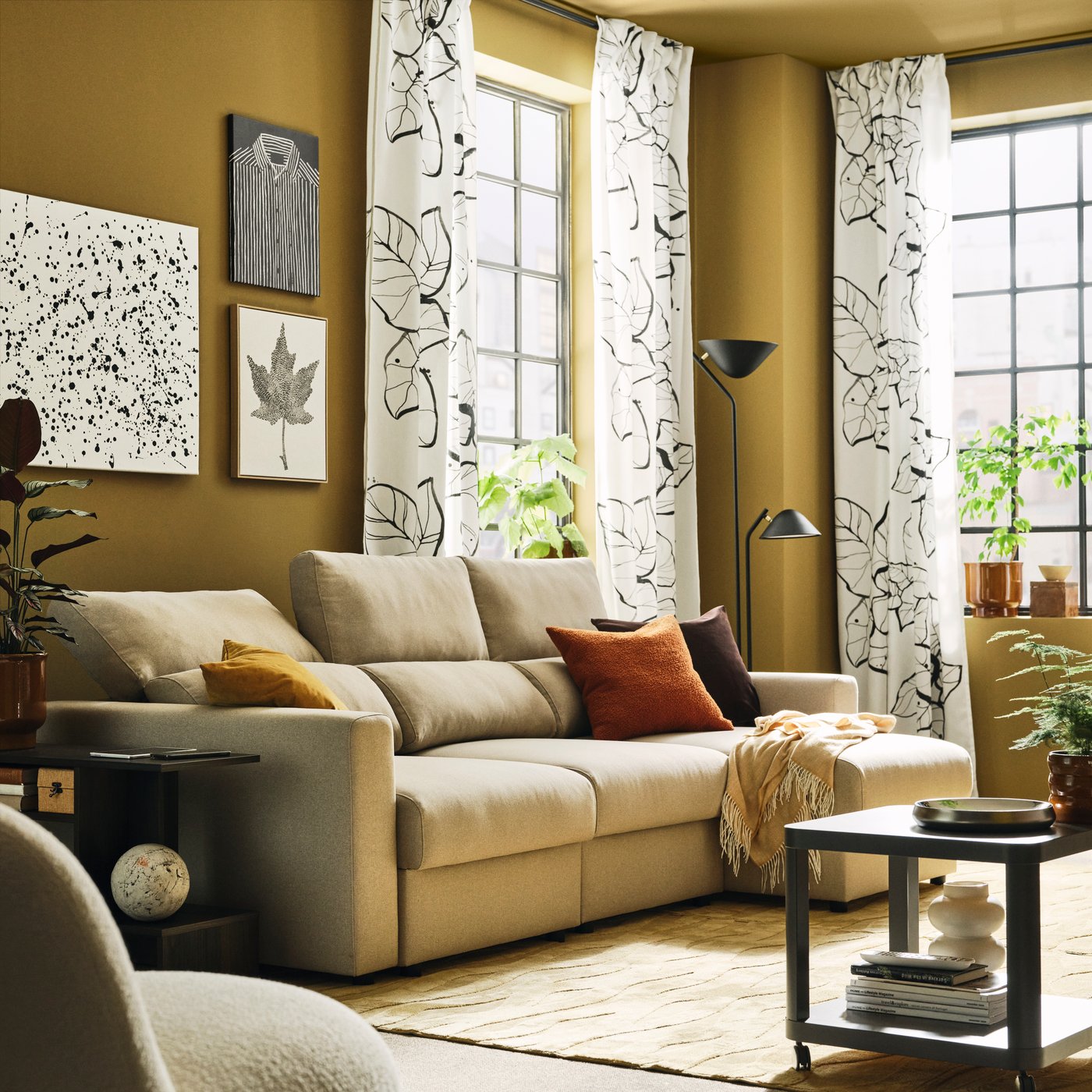 A light living room with a light-beige MALMKÖPING three-seat sofa with chaise longue flanked by side tables and plants.
