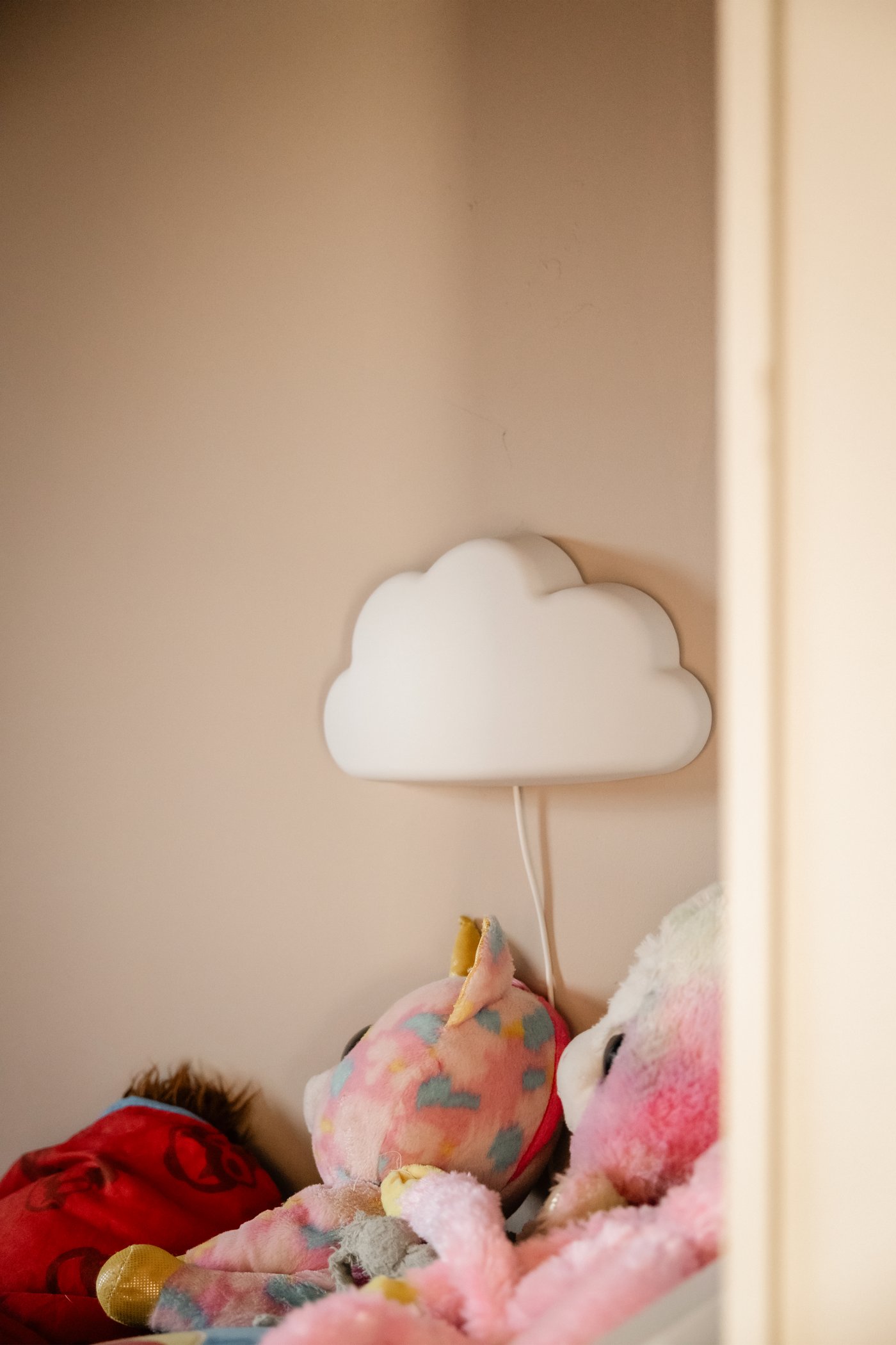Close-up foto van een kinderkamer met knuffels en een UPPLYST wolkenlamp aan de muur.
