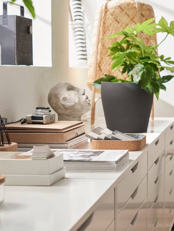 A KNIXHULT table lamp, a houseplant and various decorative items on top of four, white ALEX drawer units.