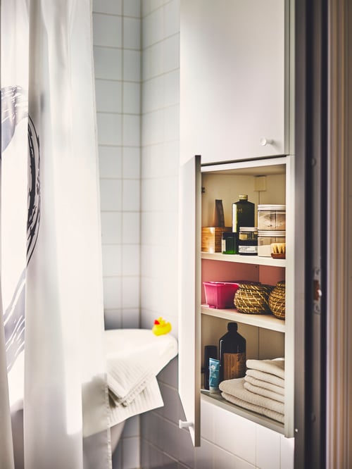 Nahaufnahme eines Badezimmers mit einem ENHET Wandschrank, FRYKEN Körben mit Deckeln und einem LYKTFIBBLA Duschvorhang.