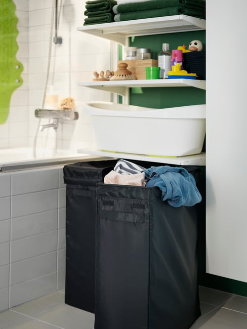 Bathroom with two laundry bags, one with stand, the other open with clothing items, and a baby bath on shelves.