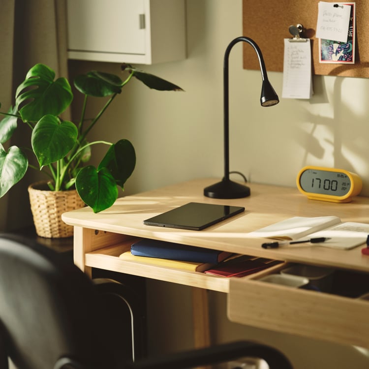 A light bamboo desk with a laptop, clock and green plant